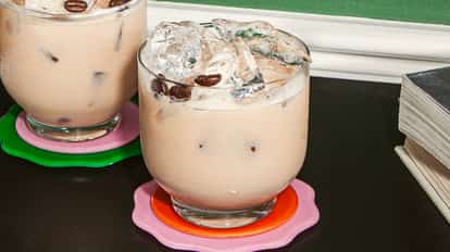 Cócteles Muddy Water en vasos redondos y fríos con hielo y granos de café como decoración, sobre posavasos coloridos en una mesa oscura.