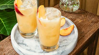 Cócteles Peach on the Beach en vasos highball con rodajas frescas de durazno sobre una bandeja de mármol.