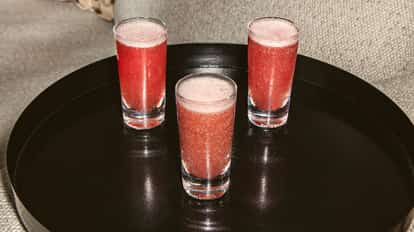 Tres shots Purple Haze en vasos pequeños transparentes, con mezcla rosada espumosa sobre una bandeja negra brillante.