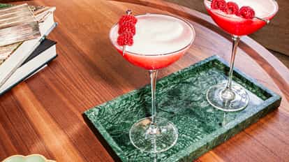 Raspberry Martinis in elegant glasses garnished with fresh raspberries on a green marble tray atop a wooden table.