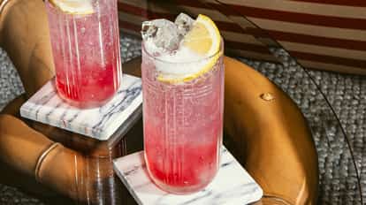 Cóctel Red Tonic en vaso alto estriado con hielo y gajo de limón, bebida roja burbujeante sobre posavasos de mármol.