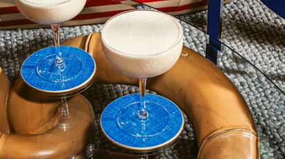 Cóctel Russian Bear en copas coupe con espuma blanca cremosa, sobre posavasos azules en mesa de cristal.