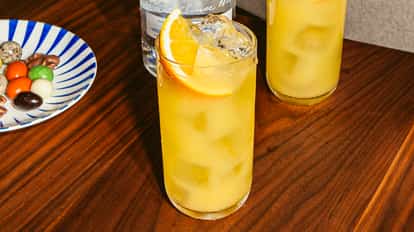 Cóctel Screwdriver en vaso alto con hielo y rodaja de naranja, bebida naranja brillante sobre mesa de madera.