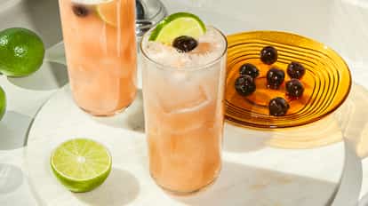 Due cocktail Sex on the Beach con ghiaccio, lime e ciliegie su piano di marmo accanto a piatto ambrato con ciliegie scure.