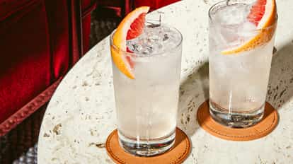 Cóctel Summertime en vasos altos con hielo y rodaja de pomelo, bebida clara y refrescante sobre mesa de piedra.