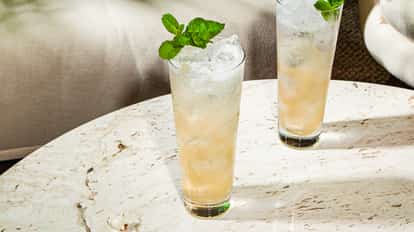 Cóctel Swedish Death Nettle en vaso alto con hielo y menta fresca, bebida dorada clara sobre mesa de piedra.