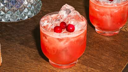 A Sweetheart cocktail in a short glass with crushed ice and bright red cranberries, showing a vibrant pink-red drink on a wooden table.