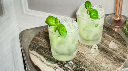 Cócteles Vodka Basil Smash en vasos fríos con albahaca fresca y hielo sobre una bandeja redonda de piedra.