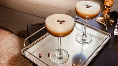 Cócteles Vodka Espresso en copas coupé con granos de café sobre una bandeja espejada junto a un sofá.
