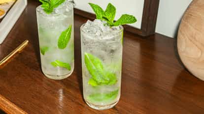 Two vodka mojito cocktails with fresh mint leaves and crushed ice served in tall glasses on a wooden surface.