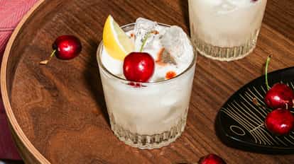 Cóctel vodka sour con hielo, rodaja de limón, cereza y bitter, servido en vaso corto sobre bandeja de madera.