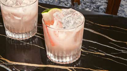 Watermelon Smash cocktail in a textured glass with ice and a watermelon wedge, standing on a dark marble tabletop.