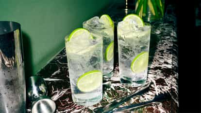 Absolut Fizzy Lemon Lime Soda in three highball glasses with ice and lime wedges on a marble countertop