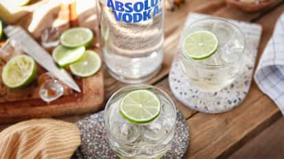 Absolut Vodka Gimlet in a rocks glass with ice and a lime wheel on a wooden table with a vodka bottle behind