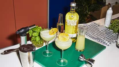 Basil Lemon Drop Martini in two coupe glasses with grilled lemon wheels and an Absolut Citron bottle on a cutting board