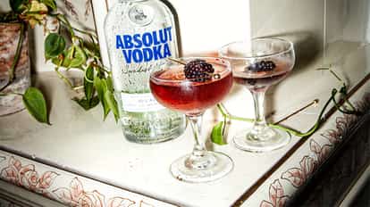 Blackberry Martini in two coupe glasses with blackberries on picks beside an Absolut Vodka bottle