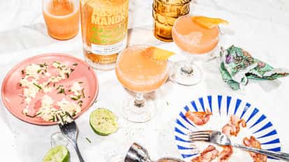 Blood Orange Cosmo served in two coupe glasses with orange twists beside an Absolut Mandrin bottle.