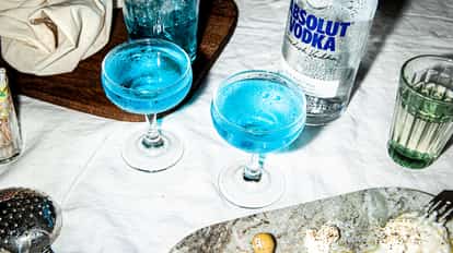 Blue Dolphin Martini served in two coupe glasses with an Absolut vodka bottle behind.