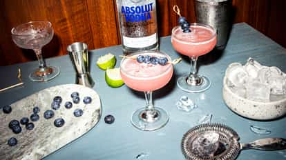 Blue Raspberry Martini in a coupe glass with a blueberry skewer and an Absolut Vodka bottle in the background