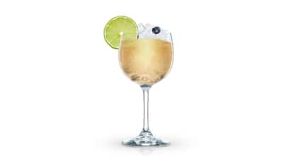 Border Crossing in a stemmed wine glass with crushed ice and a lime wheel on white background.