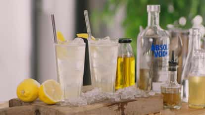 Business Time two iced tall glasses with lemon wedges and straws on board with Absolut Vodka bottle at right