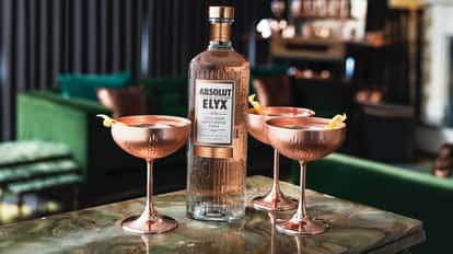Copper Bullet with an Absolut Elyx bottle and three coupes with lemon twists on a stone table