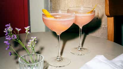 Cosmopolitan served in two coupe glasses with citrus peel garnishes.