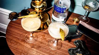 Elderflower & Pear Martini in 2 coupe glasses with pear slice garnishes beside an Absolut Vodka bottle on a wooden table