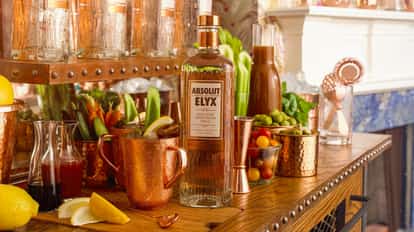 Elyx Bloody Mary in a copper mug with celery stalk and lemon wedge and a bottle behind on a wooden bar