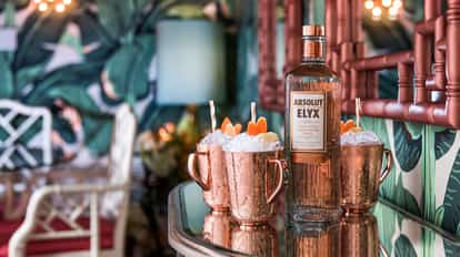 Elyx Redhead in three copper mugs with crushed ice and citrus garnish beside an Absolut Elyx bottle on mirrored bar