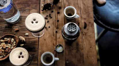 Espresso Button Fly in a coupe with three coffee beans on foam beside an Absolut bottle and espresso cups on wood