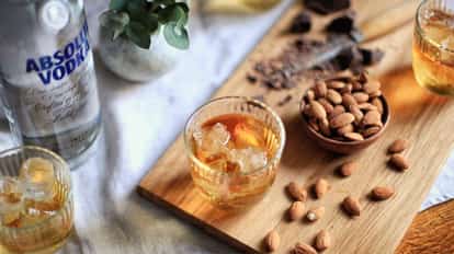 Godmother in a ridged rocks glass with ice on a wooden board beside a bowl of almonds and Absolut Vodka bottle