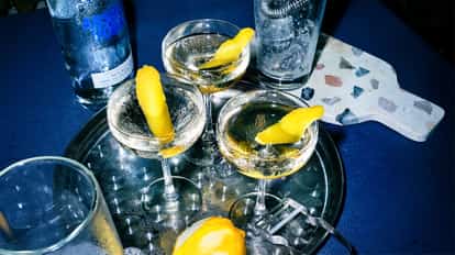Good Dill Hunting cocktails sit in three coupe glasses with lemon twists beside an Absolut bottle on a tray.