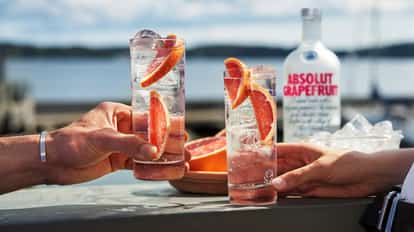 Grapefruit Vodka Tonic in highball glasses with ice, grapefruit wedges and an Absolut Grapefruit bottle behind
