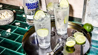 Hard Seltzer Drink in two highball glasses with ice and lime slices beside an Absolut Vodka bottle on tiles