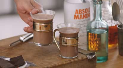 It's not Terry's in two glass mugs with metal holders on a wooden board with an Absolut Mandrin bottle in the background
