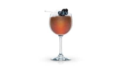 Jamaican Cobbler in a stemmed wine glass with crushed ice and blackberry and blueberries on a pick on white background