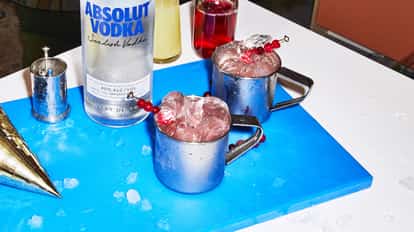 Jingle Mule in two hammered metal mule mugs filled with crushed ice and a cranberry skewer, Absolut Vodka bottle at left