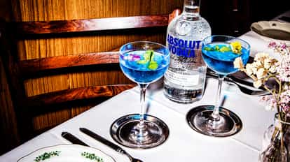 Lotus Flower Martini in coupe glasses with mint and edible flower garnish and an Absolut Vodka bottle on a tablecloth