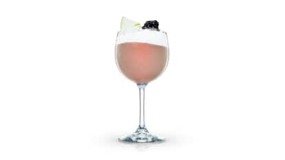 Marshall de Mure in a stemmed wine glass topped with foam and a blackberry and apple slice on white background