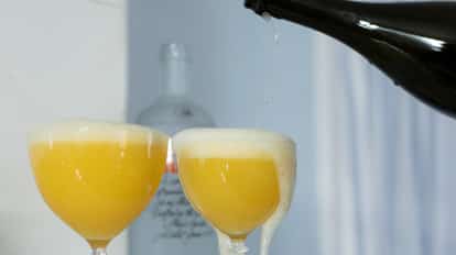 Matilda in two coupe glasses with foamy heads as a bottle pours into the right glass