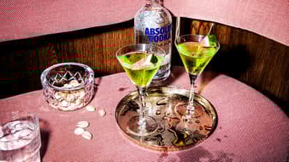 Melon Martini in martini glasses with melon wedges on a metal tray and an Absolut Vodka bottle behind