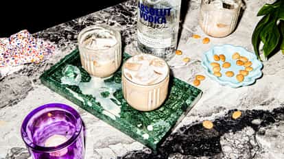 Mud Slide in a lowball glass with ice on a marble tray beside a bottle of Absolut Vodka and almonds