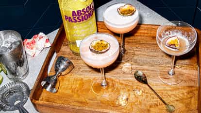 Three martinis in coupe glasses garnished with halved passionfruit and an Absolut Passion bottle.