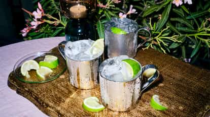 Pear and Elderflower Mule served in three metal mule mugs with ice and lime wedges on a wooden board