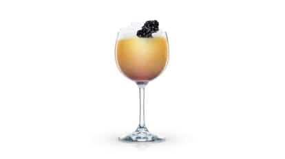 Polish Spring Punch served in a wine glass with crushed ice topped with blackberries on white background