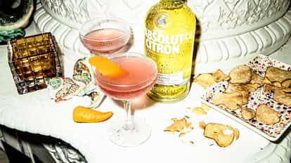 Pomegranate Martini in a coupe glass with an orange twist and an Absolut Citron bottle on a white surface