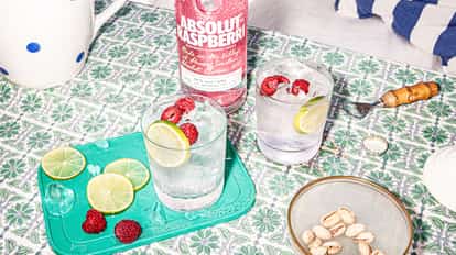 Raspberry Vodka Tonic in rocks glasses garnished with lime wheels and raspberries beside an Absolut bottle.