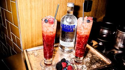 Russian Spring Punch in two glasses with crushed ice and berry garnish on a tray beside an Absolut bottle