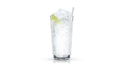 A tall highball glass holds a clear drink, crushed ice, a lime wedge and a straw on white background.